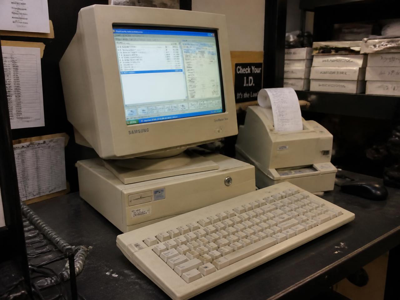 An old beige POS terminal and receipt printer on a cluttered retail back-office counter